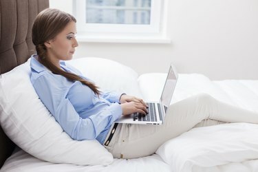 Поглед изблиза на жену која користи лаптоп на свом кревету