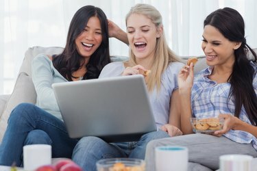 Amigos rindo, olhando para o laptop juntos e comendo biscoitos