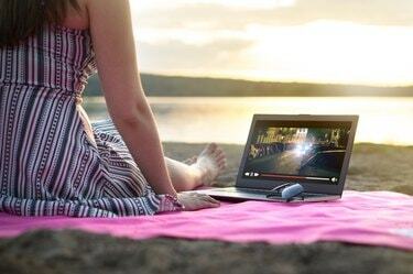 Mlada ženska pretaka film s prenosnim računalnikom na plaži ob sončnem zahodu. Gledanje filmskega toka v namišljeni spletni storitvi na prostem. Video predvajalnik na zaslonu.