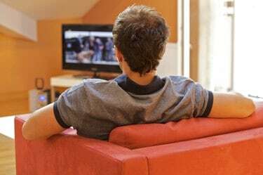 Вид сзади молодого человека, смотрящего телевизор на красном стуле