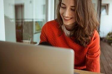 Χαμογελαστή νεαρή γυναίκα που χρησιμοποιεί φορητό υπολογιστή στο μπαλκόνι