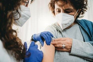 Bir kadın doktor bir bayana Covid-19 Coronavirus'a karşı aşı yapıyor.