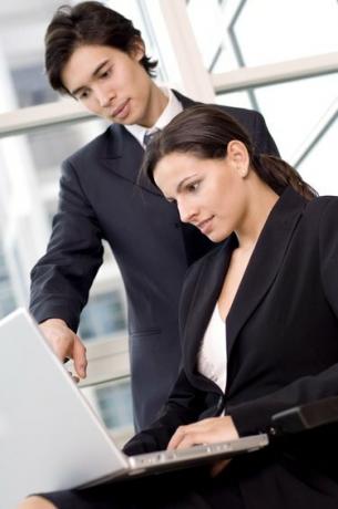Sideprofil av en forretningskvinne og en forretningsmann som ser på en bærbar datamaskin
