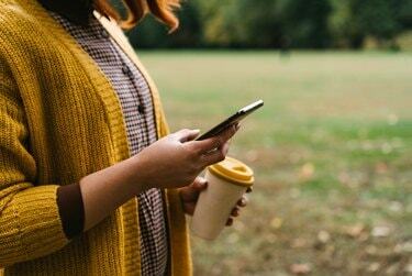 Uma mulher ruiva está caminhando no parque e segurando uma xícara de bambu com café quente