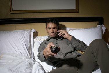 Bărbat întins pe pat, uitându-se la televizor
