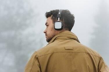 Horizontaal portret van een jonge blanke man die in een mistige berg loopt en buiten naar muziek luistert. Achteraanzicht van blanke man met trendy jas en bluetooth-koptelefoon. Mensen, technologieconcept.