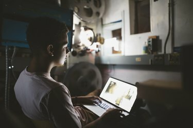 Дечак мешовите расе пројектиониста користи лаптоп у мрачном биоскопу