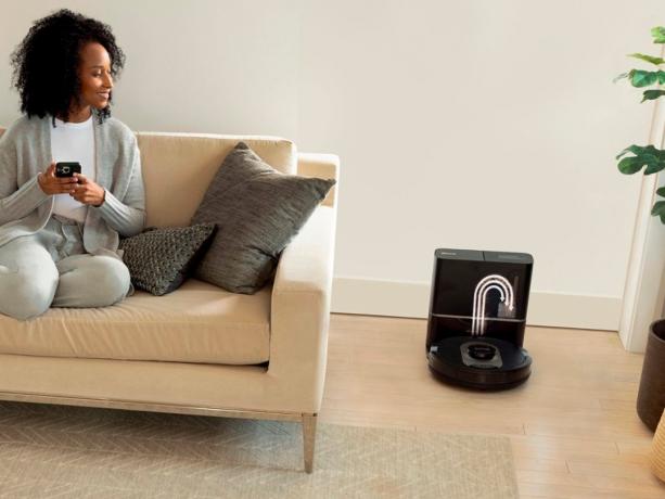 En kvinde på en sofa styrer Shark AI Ultra robotstøvsugeren med sin smartphone.