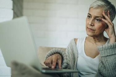 Стурбована старша жінка читає електронну пошту на ноутбуці.