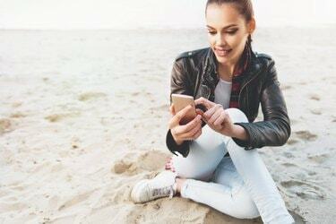 אישה צעירה וחמודה משתמשת בטלפון סלולרי על החול