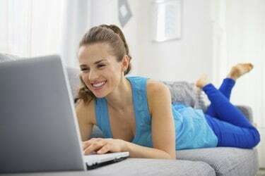 gelukkige jonge vrouw die op divan ligt en laptop gebruikt