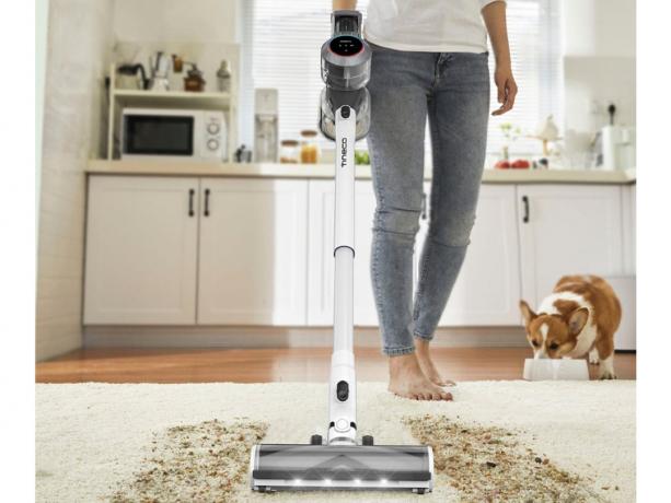 Używanie bezprzewodowego odkurzacza Tineco Pure One S11 Dual do czyszczenia zabrudzonego dywanika kuchennego, podczas gdy pies je z miski.