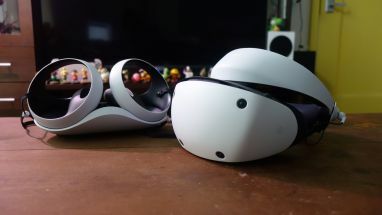 PlayStation VR2 stoji na mizi poleg krmilnikov Sense.