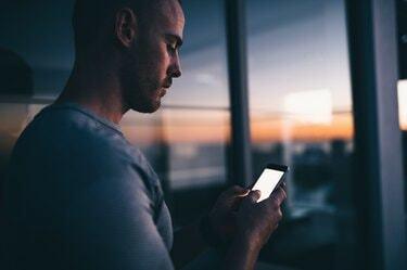 सूर्यास्त के समय मोबाइल फोन का उपयोग करते हुए आदमी का क्लोज-अप