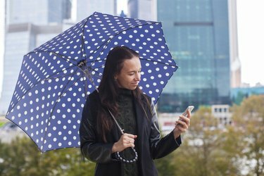 Молодая женщина разговаривает по телефону с зонтиком в руке