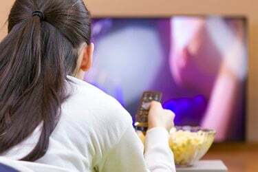Uvoľnené dospievajúce dievča s diaľkovým ovládaním sleduje inteligentnú televíziu