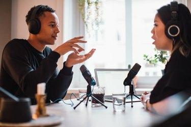 Muški bloger pokazuje ženi sa slušalicama koja sjedi za stolom