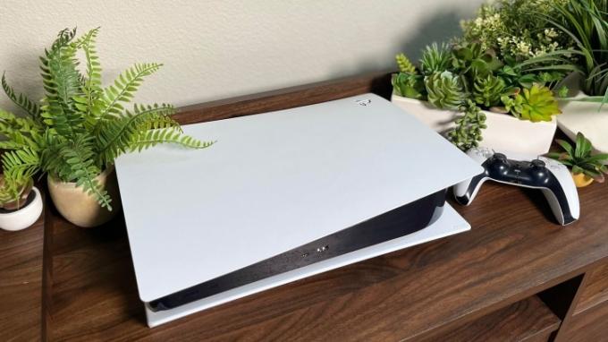 جهاز PS5 أبيض قياسي يجلس بالقرب من بعض النباتات الصغيرة في مركز الترفيه المنزلي.