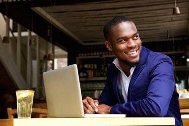 Nasmejani temnopolti poslovnež s prenosnim računalnikom v kavarni