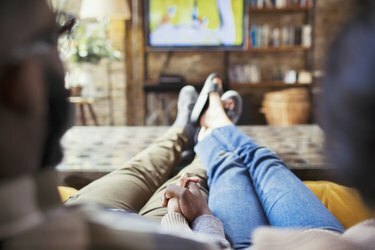 Kjærlig par holder hender, ser på TV i stuen