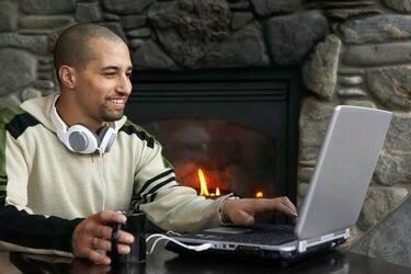 Man met koffiekopje met behulp van laptop naast open haard, glimlachend