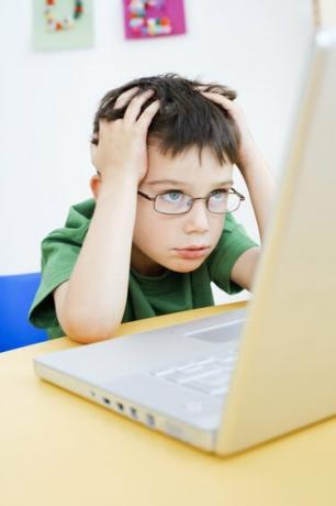 Nusivylęs berniukas, besinaudojantis nešiojamu kompiuteriu