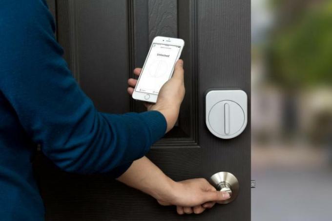 شخص يستخدم هاتفه لفتح قفل Sesame Smart Lock الموجود على باب منزله.