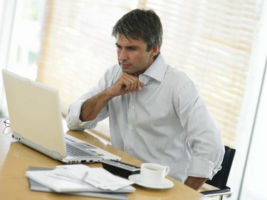 Mies pöydällä katsomassa kannettavaa tietokonetta