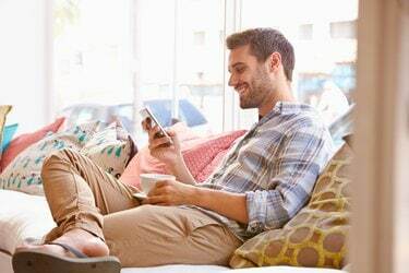 Jeune homme assis sur un canapé souriant à son téléphone