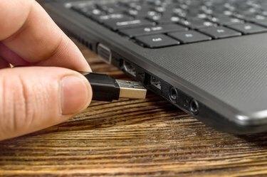 Ludzka ręka wpycha pendrive do laptopa.