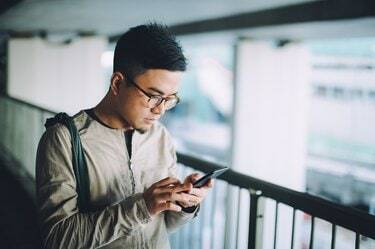 Έξυπνος νεαρός άνδρας στέλνει μηνύματα κειμένου στο κινητό τηλέφωνο στο δρόμο για δουλειά στην αστική γέφυρα στην πόλη το πρωί