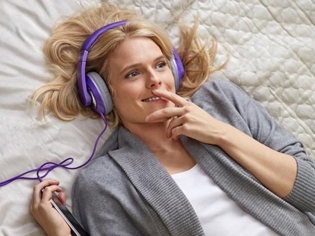 Uma mulher usando fones de ouvido e deitada na cama ouve um audiolivro Audible.