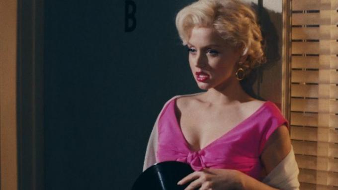 Marilyn Monroe a falnak támaszkodik, és feszülten nézi a szőkét.