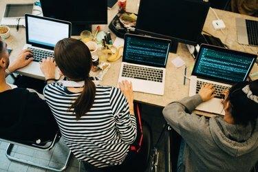 Vysoký uhol pohľadu na mladých počítačových programátorov kódujúcich na notebookoch pri stole v malej kancelárii