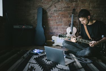 Jauns mūziķis, kas spēlē ģitāru, sēž pie piezīmju grāmatiņas