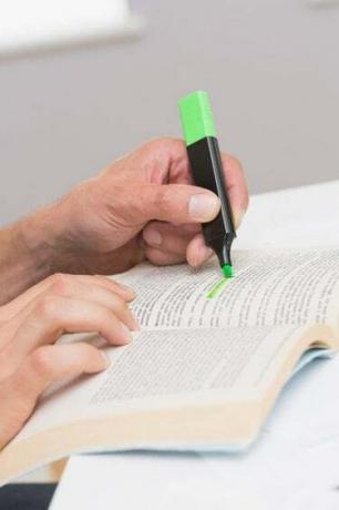 Kädet korostavat tekstiä kirjassa pöydällä