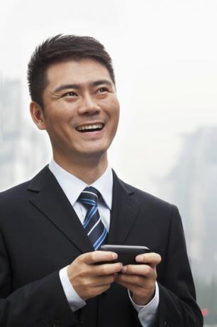 Jaunasis verslininkas šypsosi ir naudojasi išmaniuoju telefonu