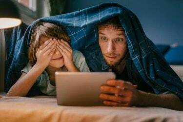 Padre e hijo emocionados viendo una película en la tableta debajo de la manta