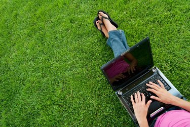 امرأة شابة باللون الوردي على جهاز الكمبيوتر المحمول الخاص بها على العشب