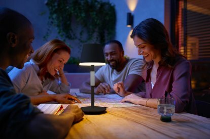 Philips Hue Go-lampa på ett uteplatsbord där vänner sitter tillsammans på natten.