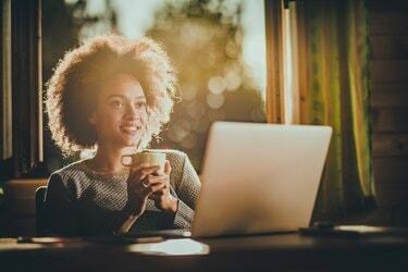 自宅でコーヒータイムにラップトップを使用しながら夢を見ている幸せな黒人女性の日。