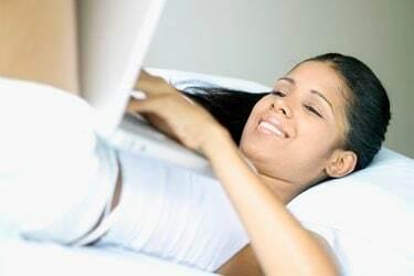 Молодая женщина, лежа с ноутбуком на животе