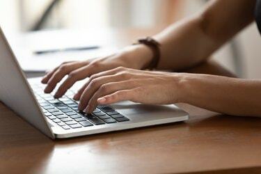 ระยะใกล้มือผู้หญิงกำลังพิมพ์บนแป้นพิมพ์โดยใช้แล็ปท็อป