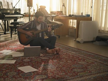 En man som spelar gitarr bredvid en bärbar dator