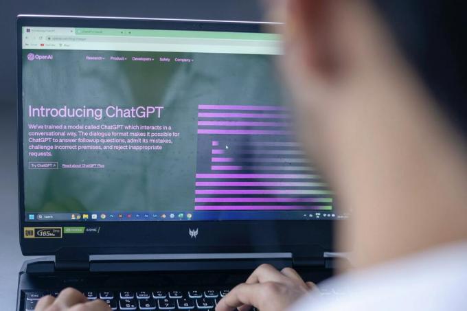 Een persoon zit voor een laptop. Op het laptopscherm is de startpagina voor OpenAI's ChatGPT artificial intelligence-chatbot.