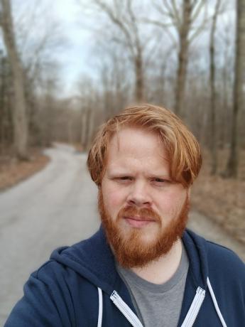 En selfie af en mand, der står på en landevej i skoven med en sløret baggrund
